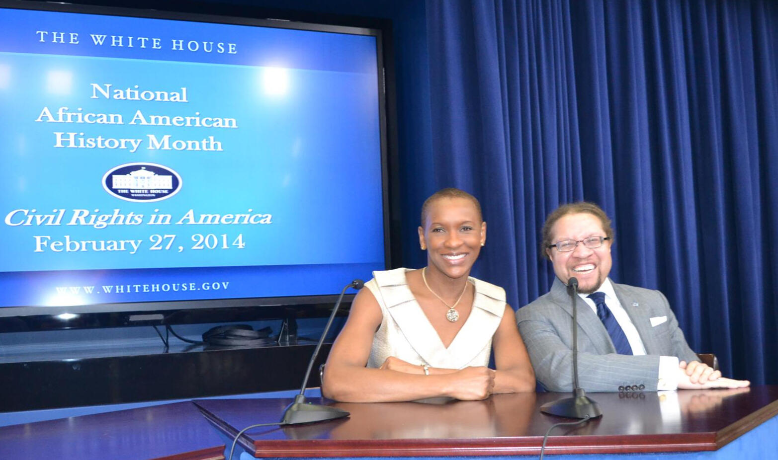 Patrick seated at a broadcast‑style desk with lights and microphones at the White House